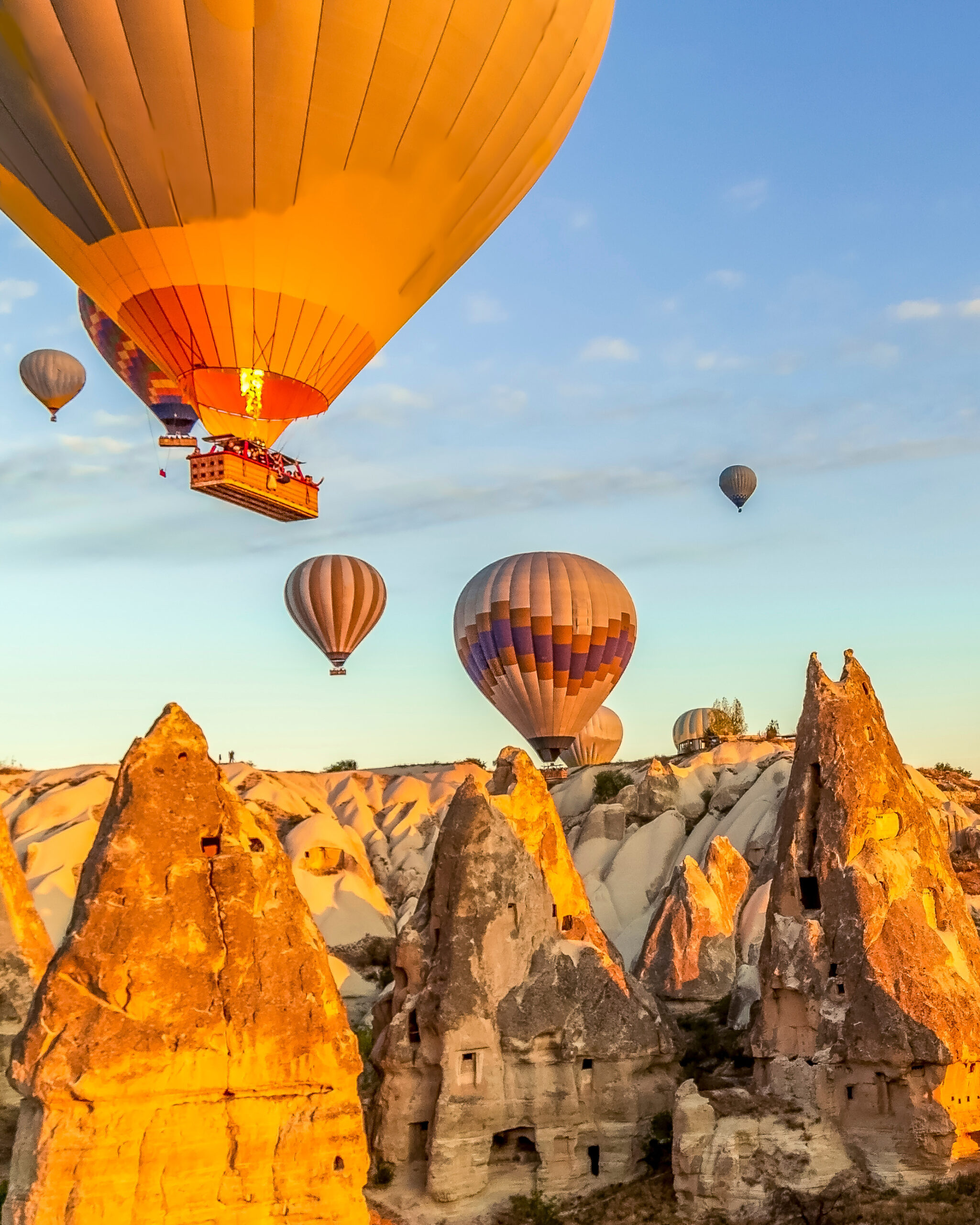 Bright morning as many hot air balloons float in clear skies just above the valleys and homes in Cappadocia